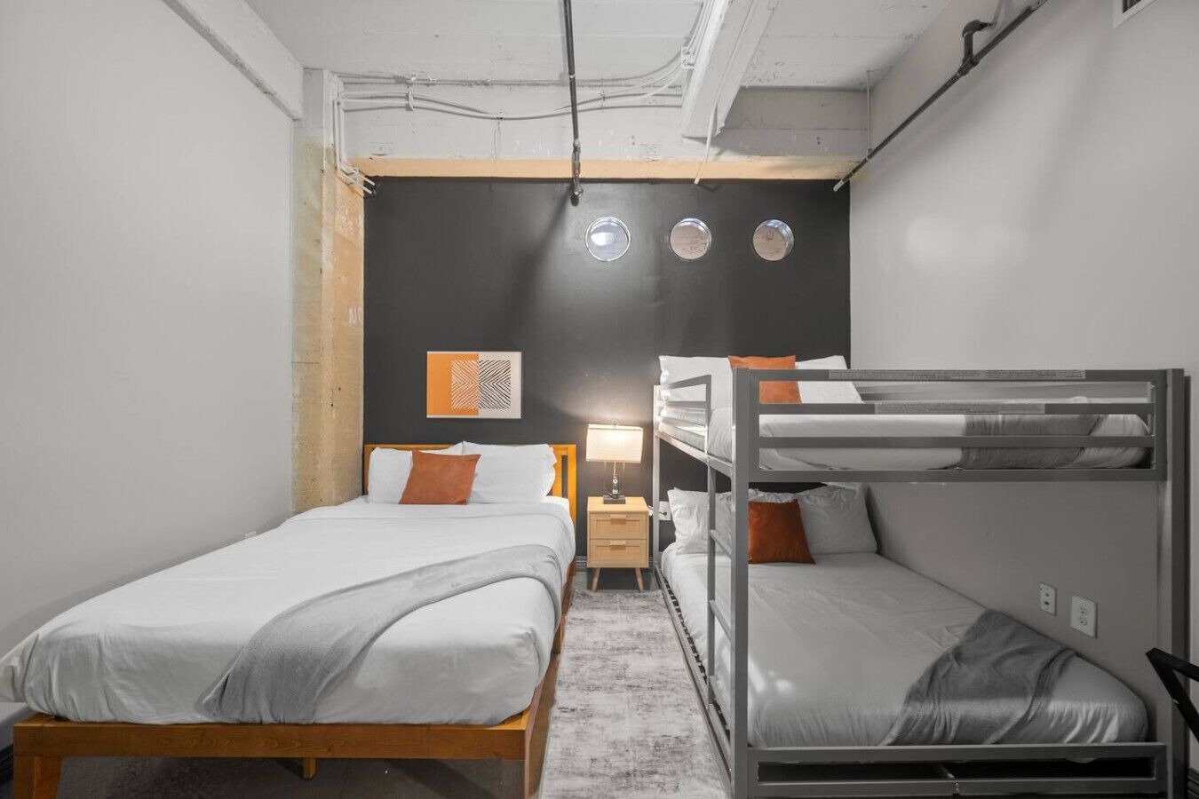 A compact hotel room with a bunk bed, a single bed, and a small bedside table with a lamp.