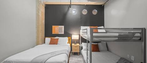 A compact hotel room with a bunk bed, a single bed, and a small bedside table with a lamp.