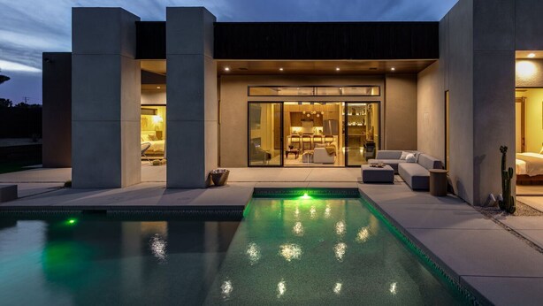 A modern house with a swimming pool, a patio area, and a well-lit interior. - Windsong | Modern compound w pool & spa (Yucca Valley)