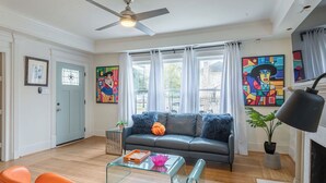 A living room with a sofa, two orange chairs, a glass coffee table, a ceiling fan, and artwork on the walls. - 7BR The Athena! Luxury Chef's Kitchen in Montrose ★★★★★ (Houston)