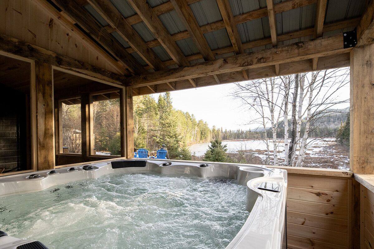 A wooden cabin with a hot tub and a view of a snowy landscape.