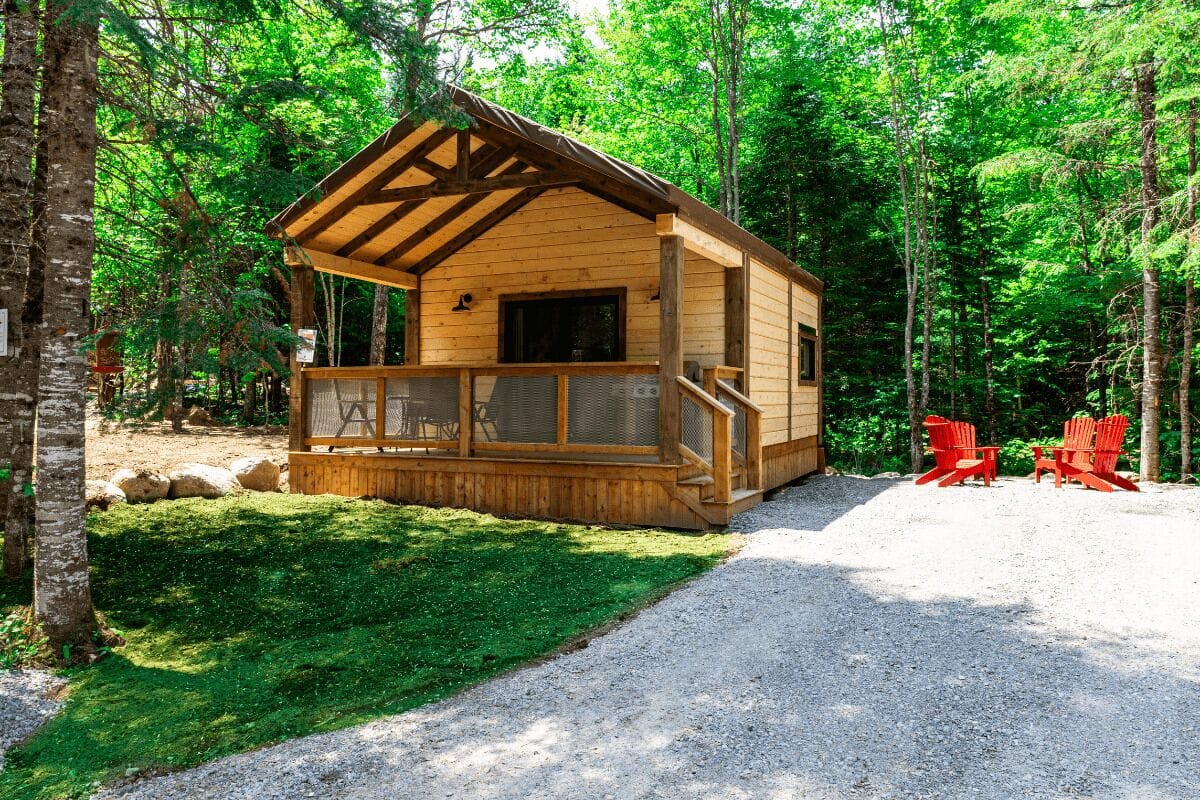 A wooden cabin with a porch, surrounded by trees.