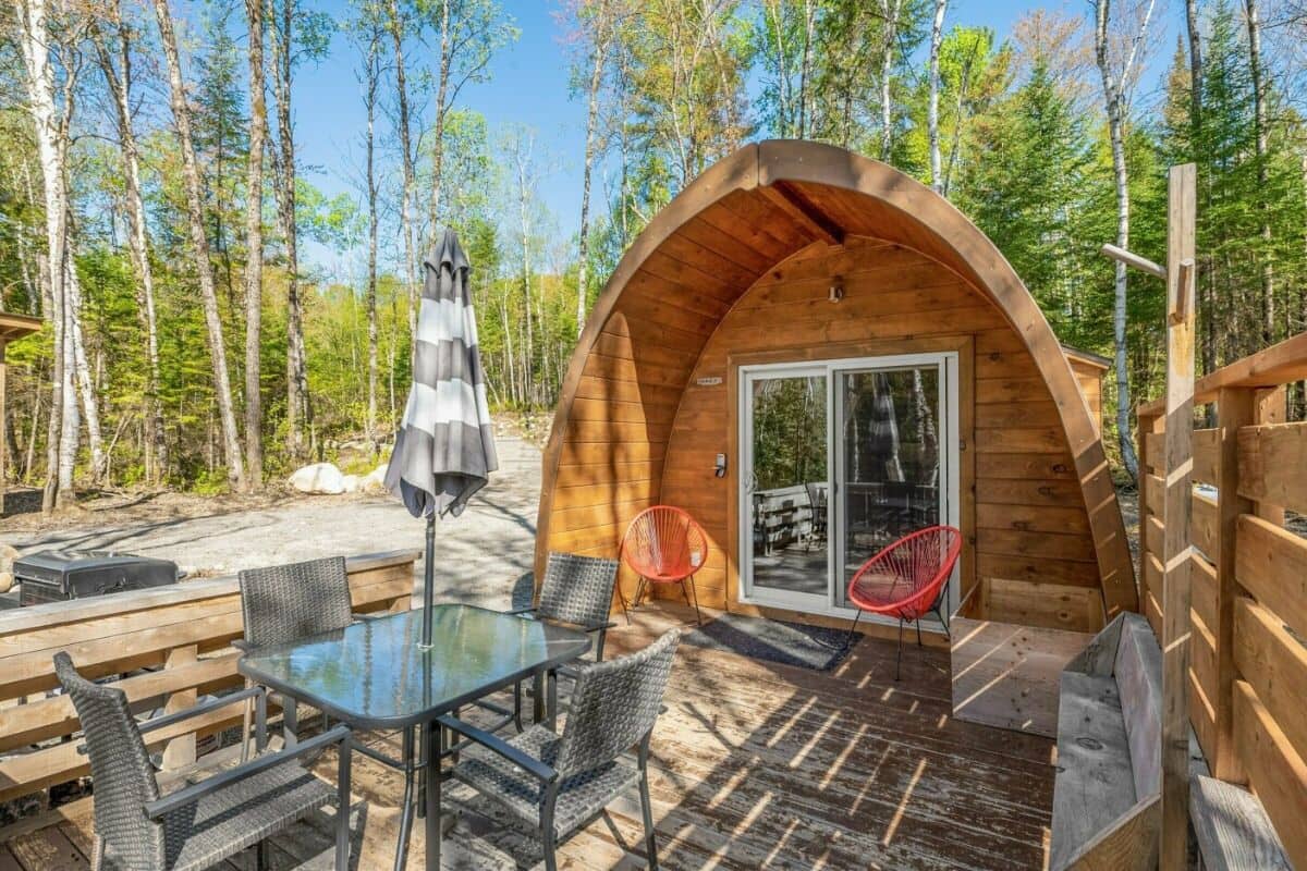 A wooden cabin with a glass door, surrounded by a deck with outdoor seating and a table.