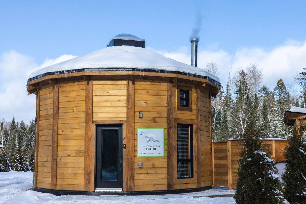 A wooden yurt with a snow-covered roof, a chimney, and a sign indicating it is a lodge.