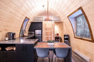 Acogedor interior de cabaña con detalles de madera, una zona de cocina con electrodomésticos modernos y una mesa de comedor con sillas.