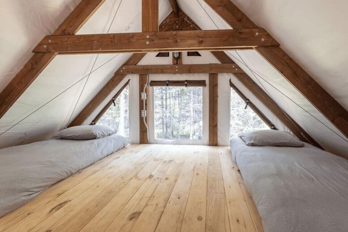 A triangular attic bedroom with wooden beams, two beds, and a view of a snowy forest.