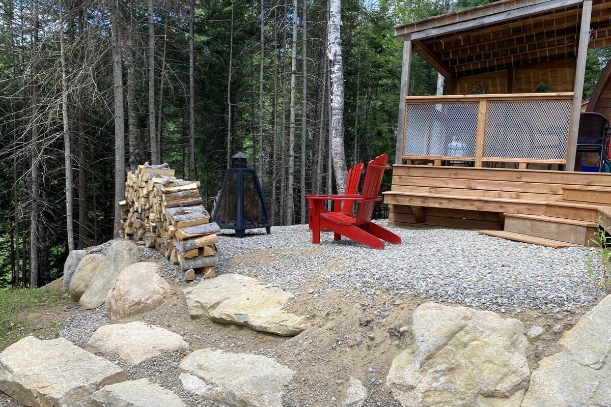 A cabin with a wooden deck, a fire pit, and a stack of firewood.