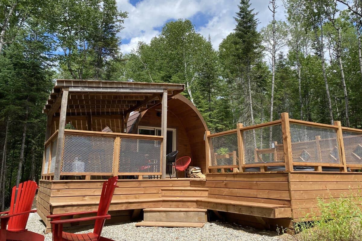 A wooden cabin with a covered porch, a red chair, and a small table.