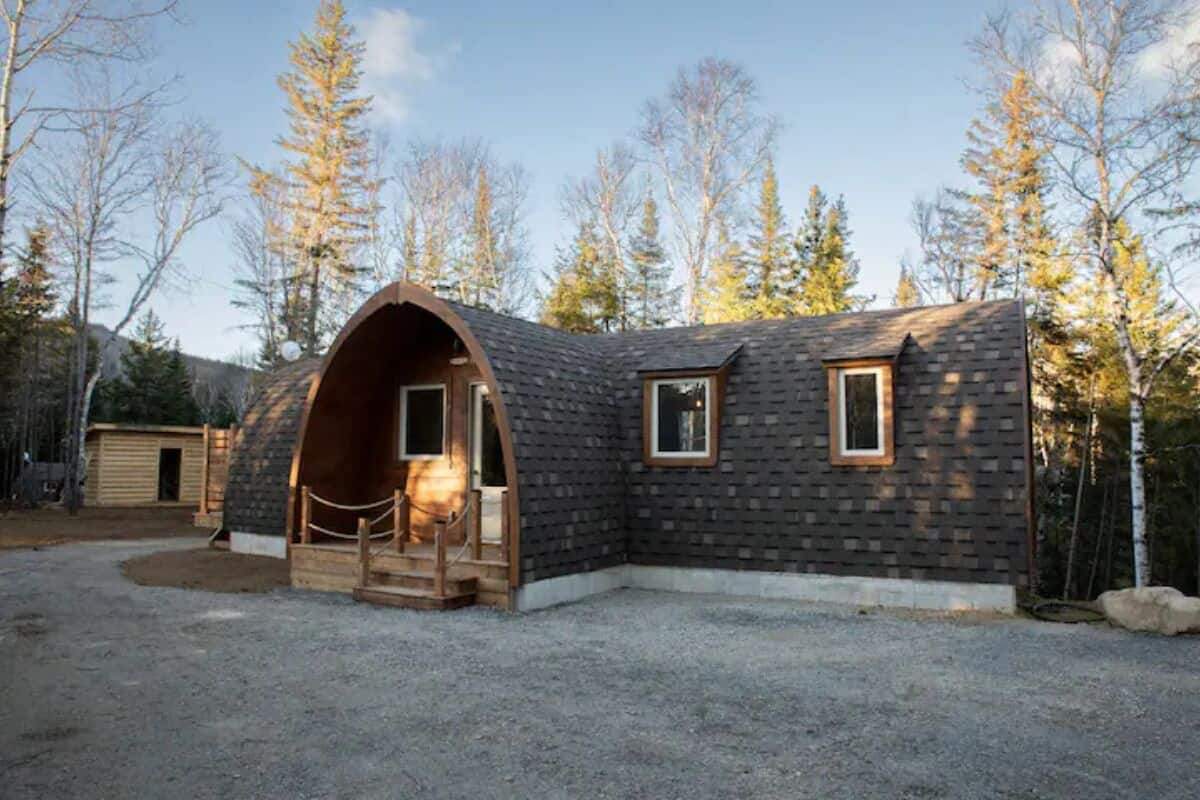 A cabin with a curved entrance, a small window, and a gravel driveway.