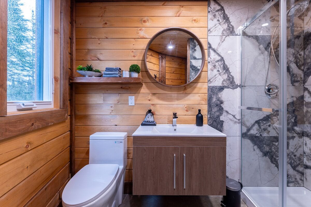 A wooden-paneled bathroom with a toilet, sink, and shower.