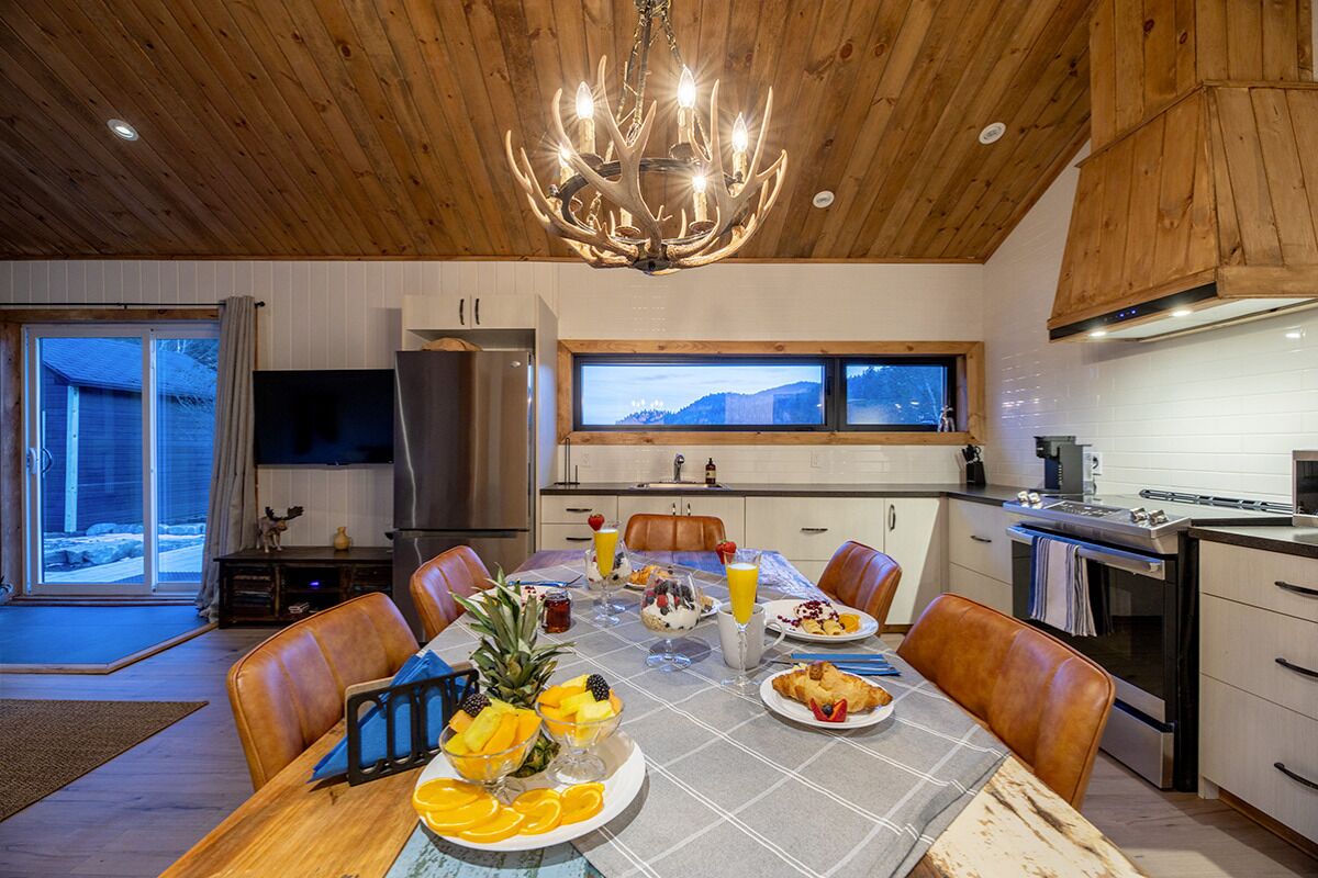 Una cocina moderna con comedor, techo de madera y un amplio ventanal con vistas a un paisaje nevado.