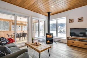 Una sala de estar moderna con una chimenea grande, pisos de madera y un televisor sobre un mueble de madera.