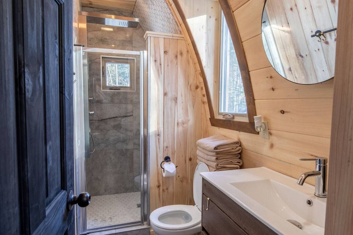 Baño de cabaña de madera con un lavamanos grande, inodoro y zona de ducha.