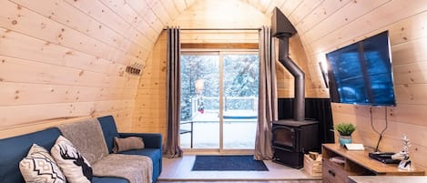 Un acogedor interior de cabaña con techo de madera, un sofá azul, chimenea y televisión en la pared.