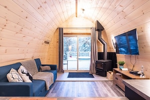 Un acogedor interior de cabaña con techo de madera, un sofá azul, chimenea y televisión en la pared.
