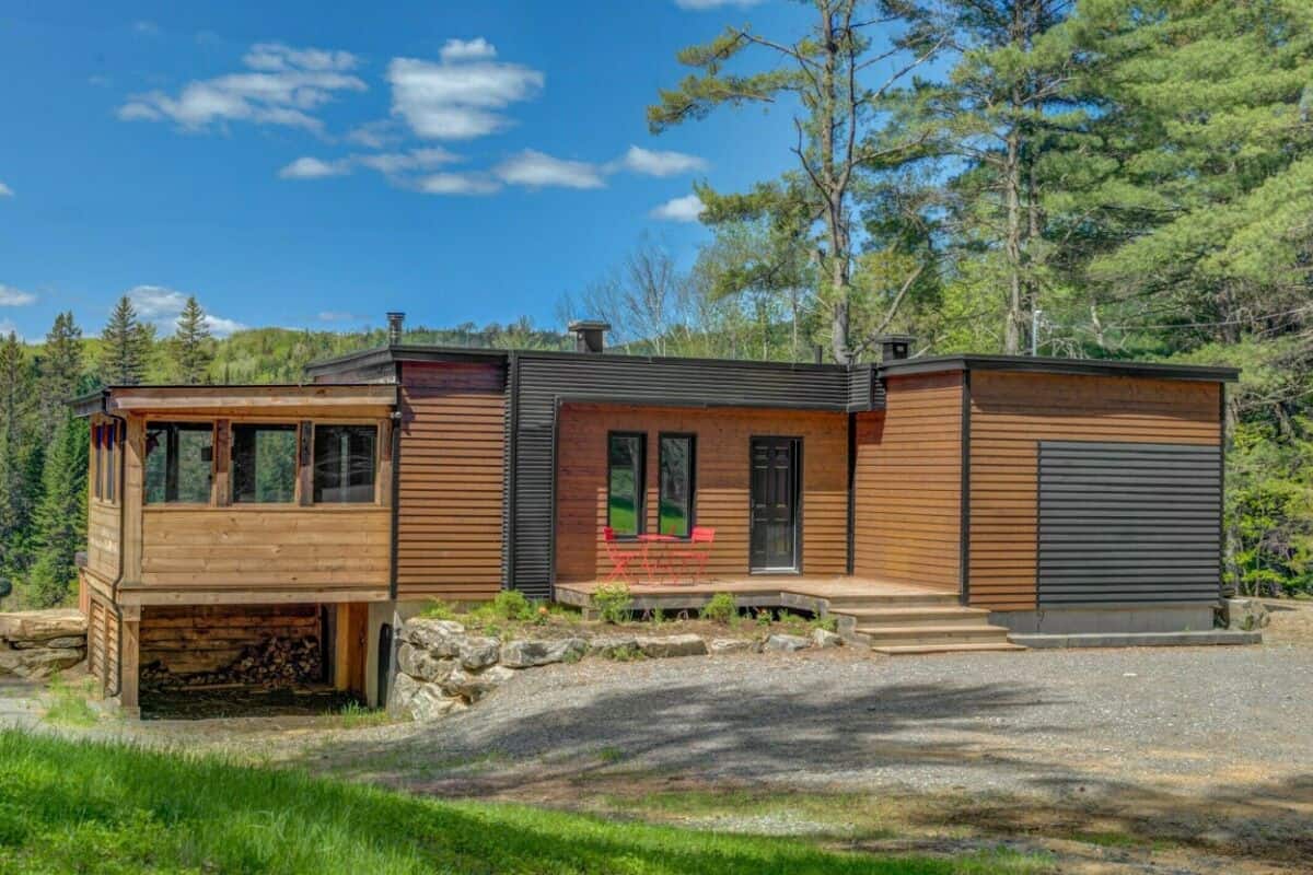 A modern log cabin with a deck, a garage, and a stone foundation.