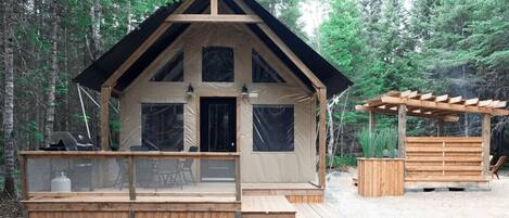 A cabin with a wooden deck, large windows, and a pergola structure.
