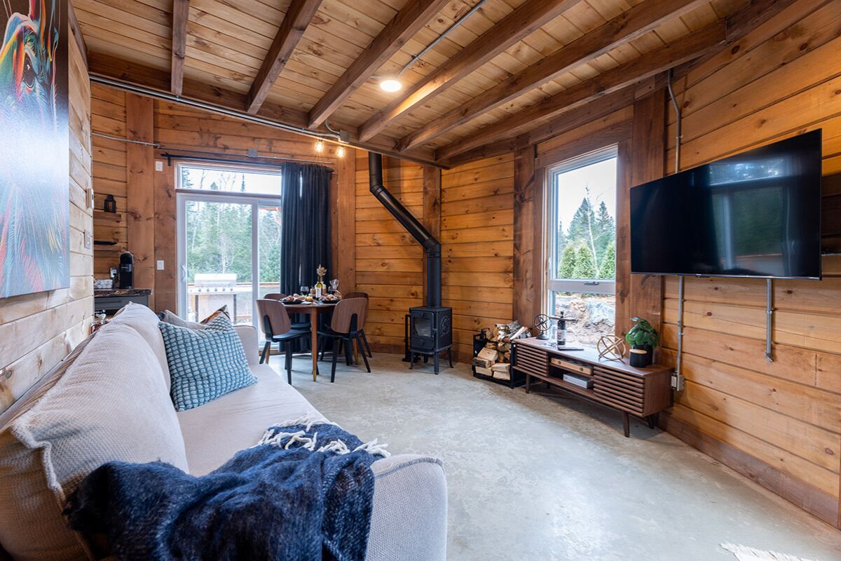 A cozy cabin interior with a sofa, TV, dining area, and a fireplace.