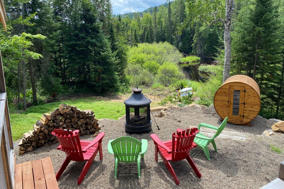 Un rincón acogedor al aire libre con sillas Adirondack, un brasero y leña.
