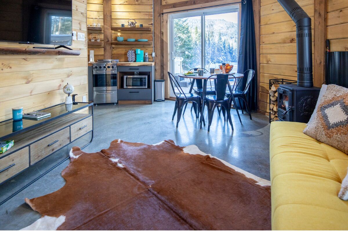 A cozy cabin interior with a dining area, kitchen, and a sofa with a cowhide rug.