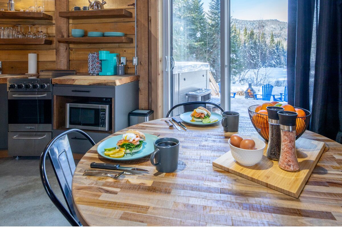 A cozy kitchen with wooden shelves, a dining table set with breakfast, and a view of a snowy landscape.