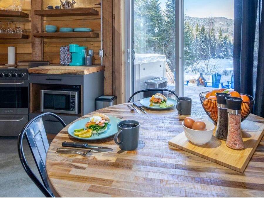 Una cocina acogedora con estantes de madera, una mesa de comedor lista para el desayuno y vistas a un paisaje nevado.