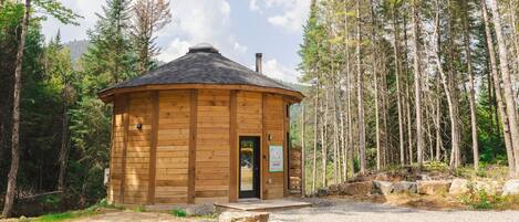 A wooden cabin with a circular roof, surrounded by trees.