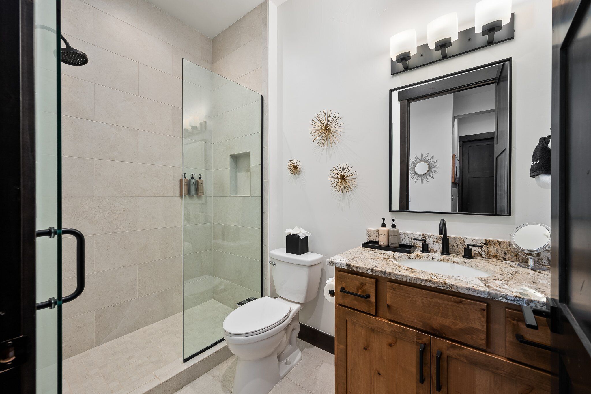 A modern bathroom with a glass shower enclosure, a toilet, and a vanity with a mirror and countertop.