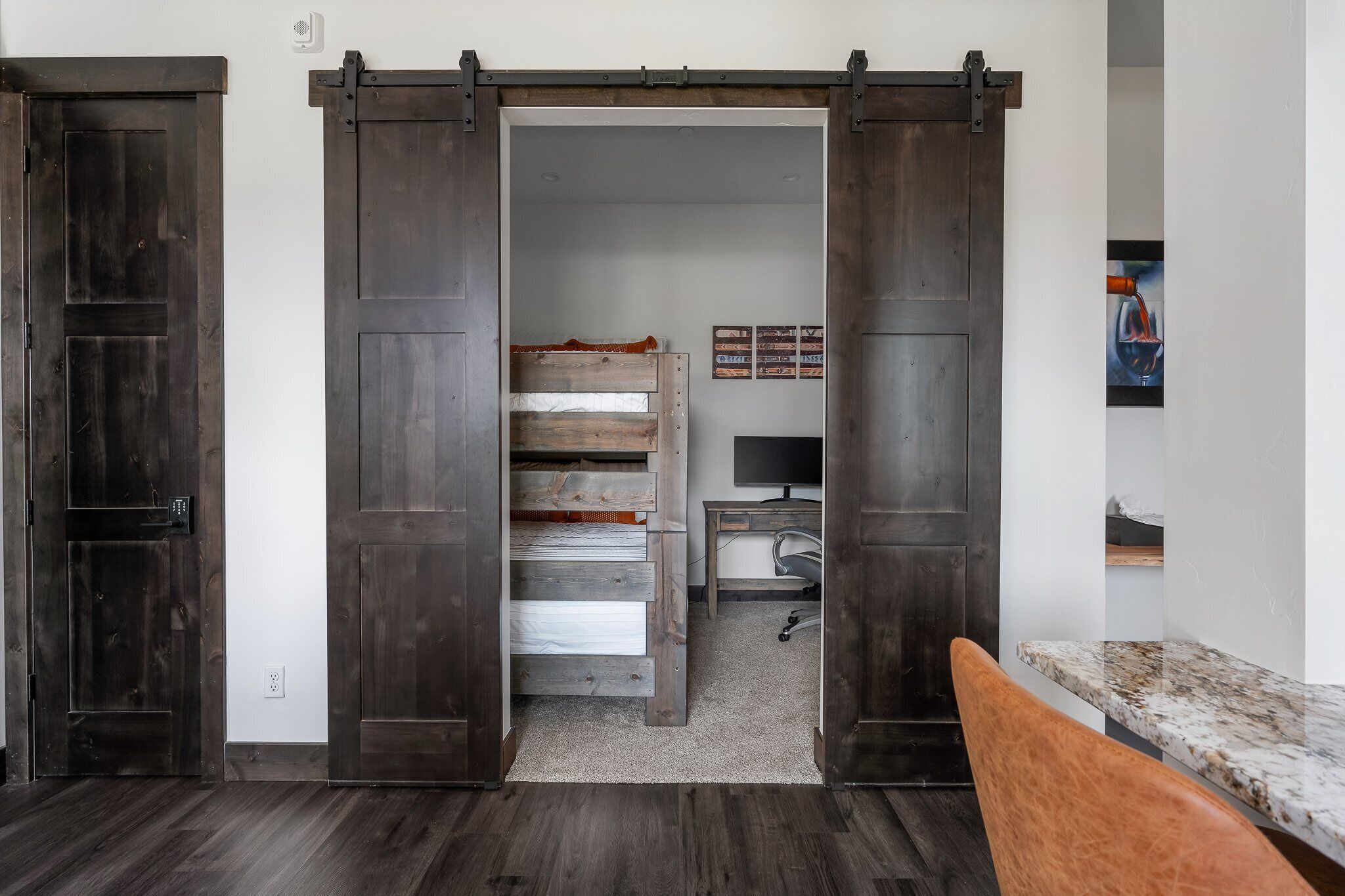 Ein Zimmer mit einer Schiebetür im Bauernhausstil, einem Bett mit Stauraum, einem Schreibtisch inklusive Computer und einer kleinen Sitzecke.