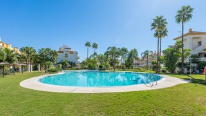 A swimming pool surrounded by grass and palm trees, with buildings in the background. - Bright Bay Calanova Grand Golf (Mijas Costa)