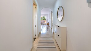 A hallway with a mirrored wall, a radiator, and a view into a room with a chair and a table. - Bright Bay Calanova Grand Golf (Mijas Costa)