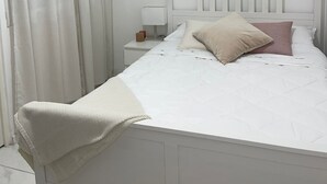 A neatly made bed with a white headboard, a bedside table with a lamp, and a window with white curtains.