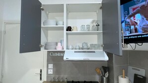 A compact kitchen with a stove, cabinets, and a TV displaying a cooking show.