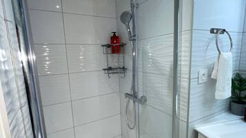 Een moderne badkamer met een glazen douchecabine, witte betegelde wanden en een klein plankje met toiletartikelen.