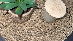 A woven placemat with a salt shaker, a candle, a small potted plant, and a remote control.