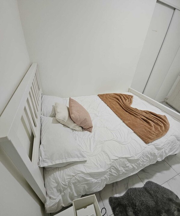 A single bed with white bedding and a brown blanket, a white radiator, and a gray rug on the floor. - 1-Joli appartement quartier saint-Anne, Reims (Reims)