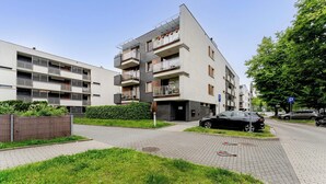 En modern lägenhetsbyggnad med flera balkonger, en asfalterad uppfart och en parkeringsplats.