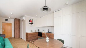 A modern kitchen with white cabinets, a wooden dining table, and a green sofa.