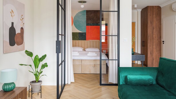A modern room with a bed, a green sofa, a potted plant, and a painting on the wall.