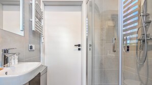 Een moderne badkamer met een douchecabine van glas, een witte wastafel en een deur naar een andere kamer.
