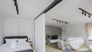 Ein modernes Hotelzimmer mit Bett, Sofa, Esstisch und Fernseher.