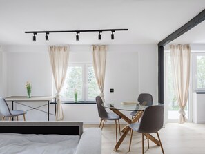 Un comedor moderno con una mesa de vidrio, sillas grises y un sistema de iluminación con rieles negros en el techo.