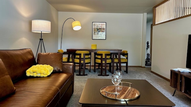 Un salon moderne avec un canapé en cuir marron, une table à manger avec des chaises jaunes, un lampadaire et un meuble pour la télévision.