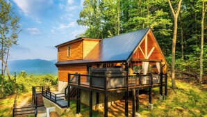 A cabin with a deck, wooden exterior, and a view of the mountains.