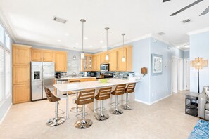 A modern kitchen with a central island, bar stools, stainless steel appliances, and wooden cabinets.