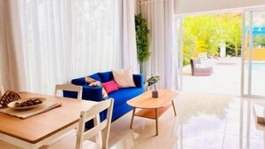 Ein großzügiger Wohnbereich mit einem blauen Sofa, weißen Sesseln, einem Holztisch und einem großen Fenster mit transparenten Vorhängen.