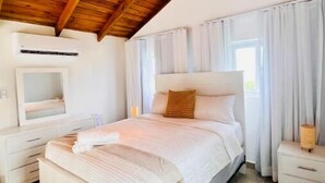 Ein Schlafzimmer mit Holzbalkendecke, einem Bett mit weißer Bettwäsche, einem Nachttisch und einem Fenster mit Vorhängen.