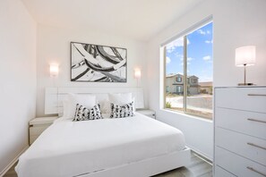 A bedroom with a large bed, a window with a view of buildings, and a wall-mounted artwork.