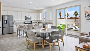 A modern kitchen with white cabinets, stainless steel appliances, and a dining area with wicker chairs.
