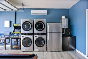 A laundry room with stacked washers and dryers, a water heater, and a small table with a chair. - Margaritaville | Pickleball, Pool+Spa, GameRoom! (Coachella)